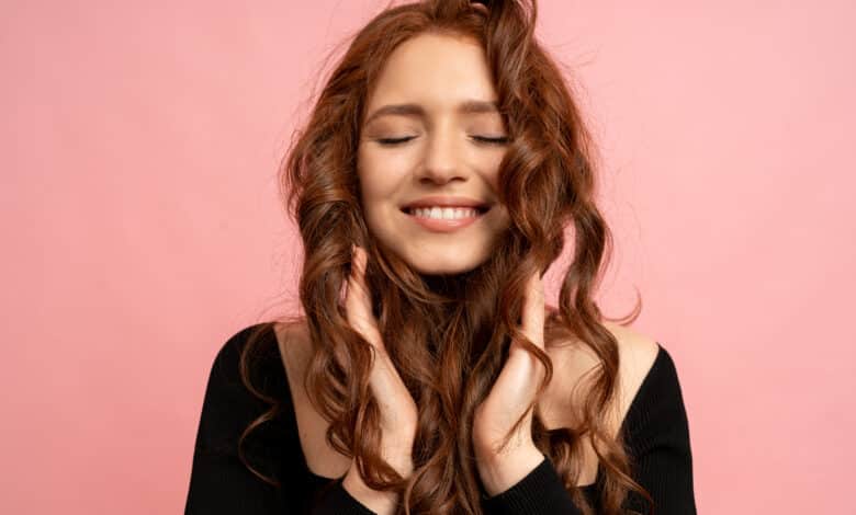 beautiful red head woman with close eyes posing pink wall wavy hairs perfect smile 1