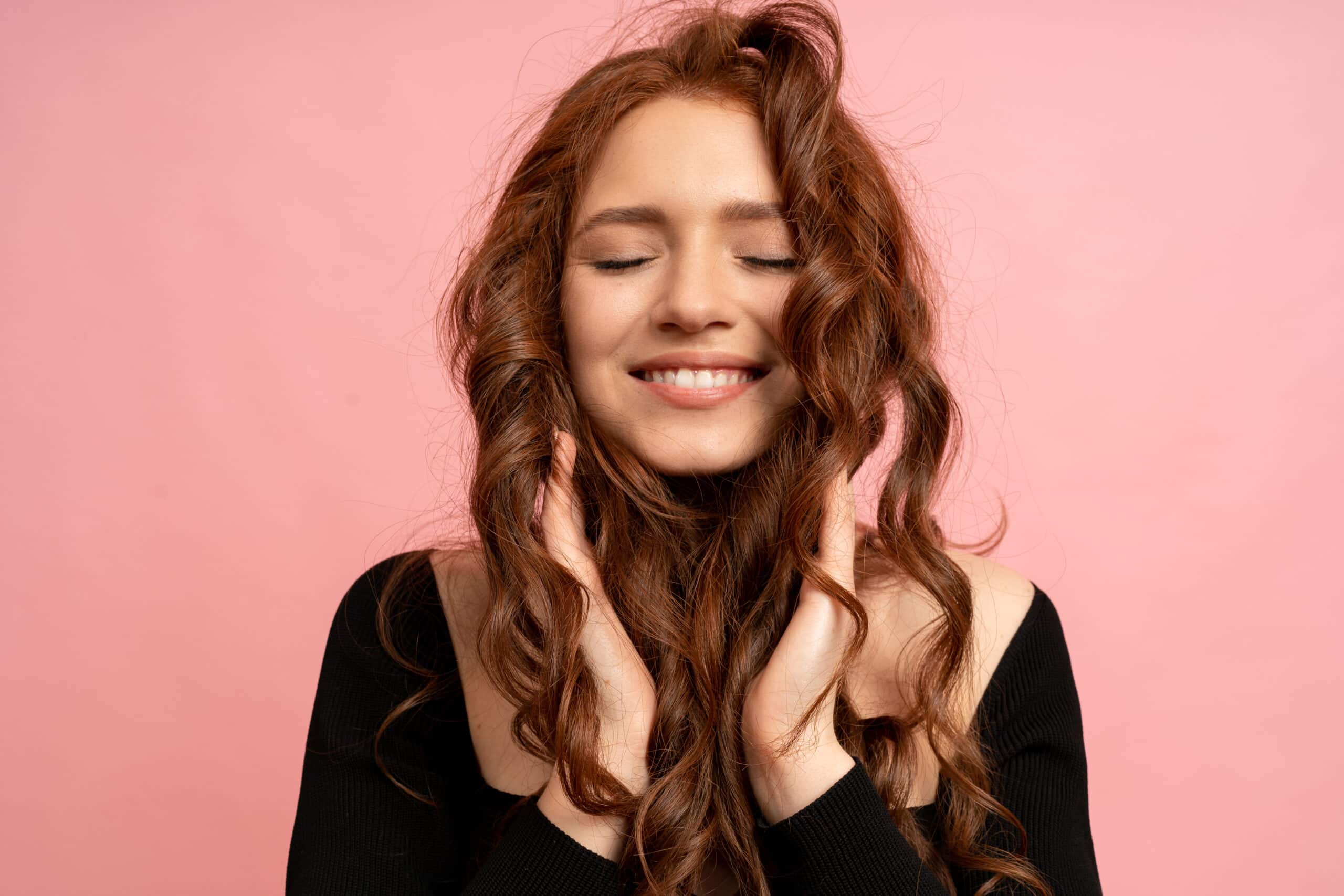 beautiful red head woman with close eyes posing pink wall wavy hairs perfect smile 1 scaled